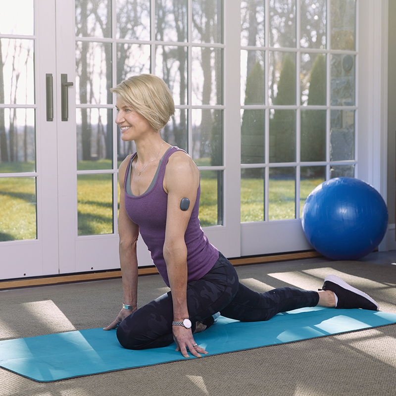 En kvinna i yogaställning med en Eversense CGM på armen.